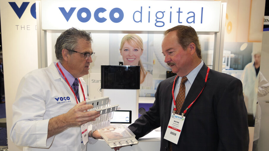Henri Paszkiewicz speaks to an attendee about the benefits of VOCO’s new SolFlex 3-D printer at the company’s booth.