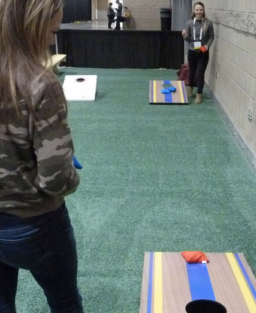 In the Expo Hall’s lawn-games area, sponsored by Peebles Prosthetics, Jill Wigle, facing camera, tosses a bean bag as Trisha Cashmore awaits her turn. Both are chairside assistants with Copeland Family Dental in Highlands Ranch, Colo.