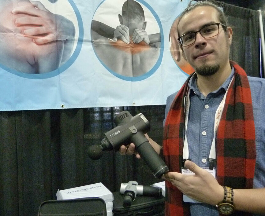 Robert Schmidt of Healthtec Industries displays a FIT 888 cordless percussive massager, one of several variations of the device being offered for sale in the Expo Hall.
