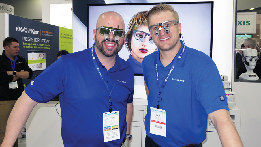Jason Clark, left, shows off the EyeZoom adjustable magnification loupe with a green laser insert, while Matt Oven wears the XVI in the Orascoptic booth. 
