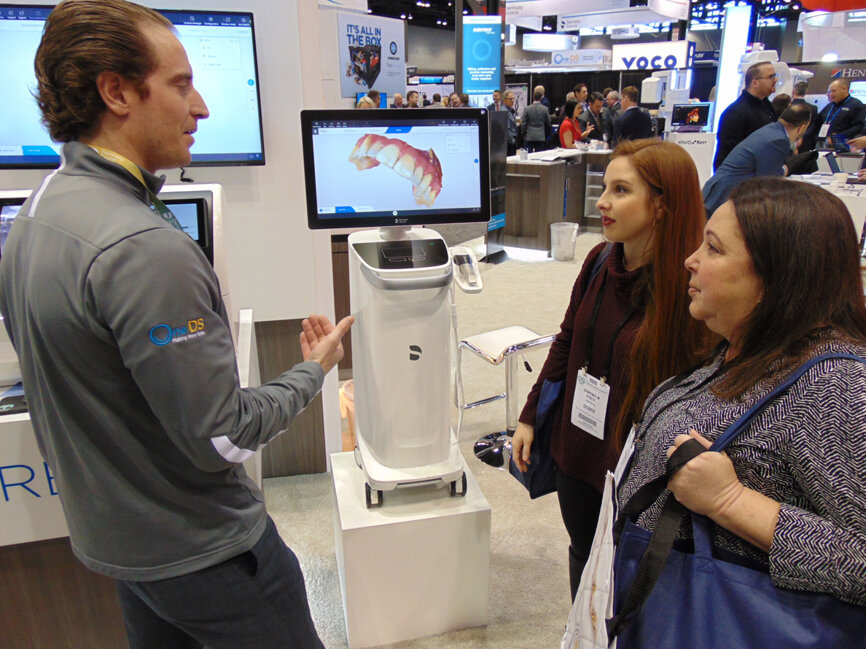 At the Henry Schein booth, Zach Bietzel explains some of the latest features and benefits of CEREC chairside dentistry to Dr. Courtney M. Stoltz and Dr. Brooke M. Stoltz. 
